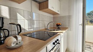 A modern kitchen with a black coffee maker, a glass kettle, and a bowl of fruit on the counter. - Holiday flat with balcony (Šilo)