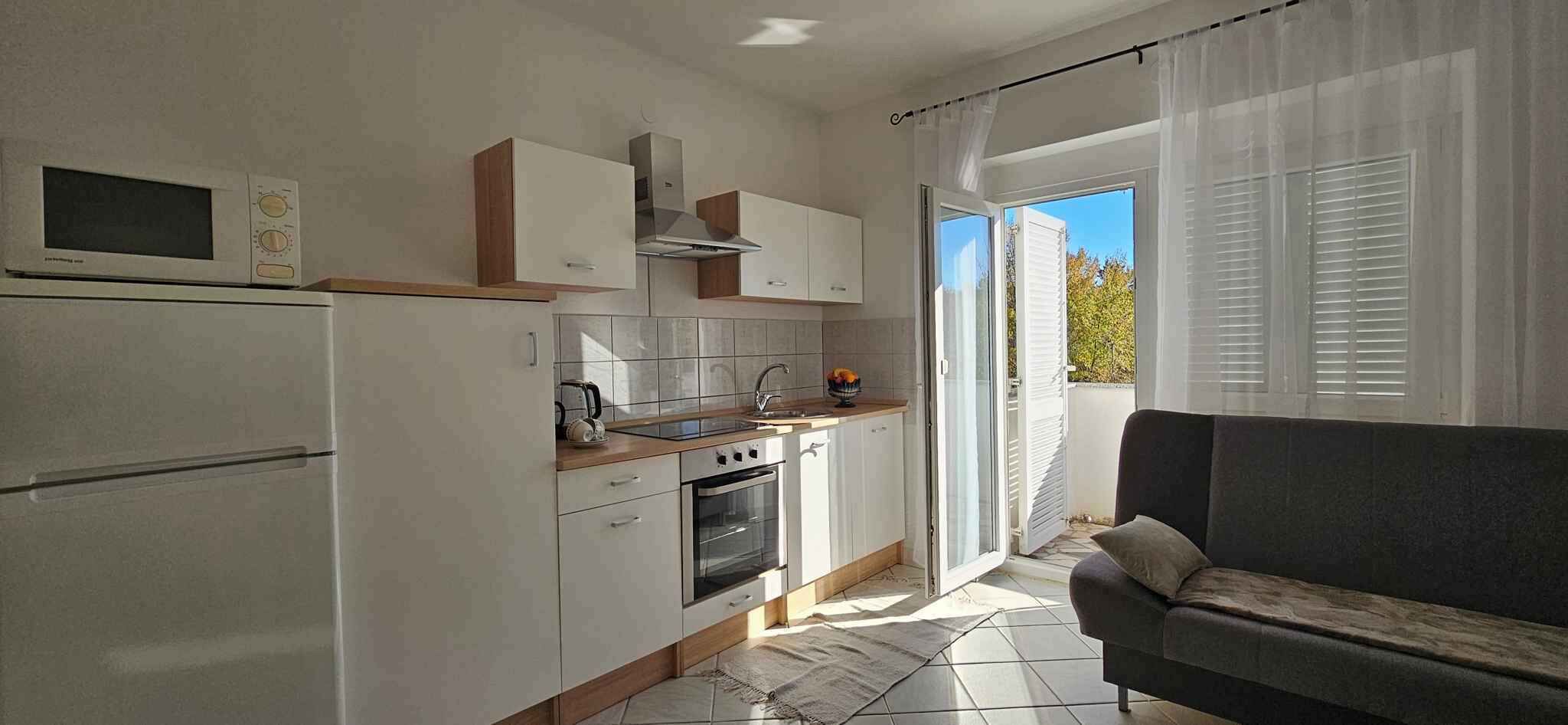 Et kompakt køkken med mikroovn, ovn og vask, beliggende ved siden af en skydedør, der fører ud til en balkon.