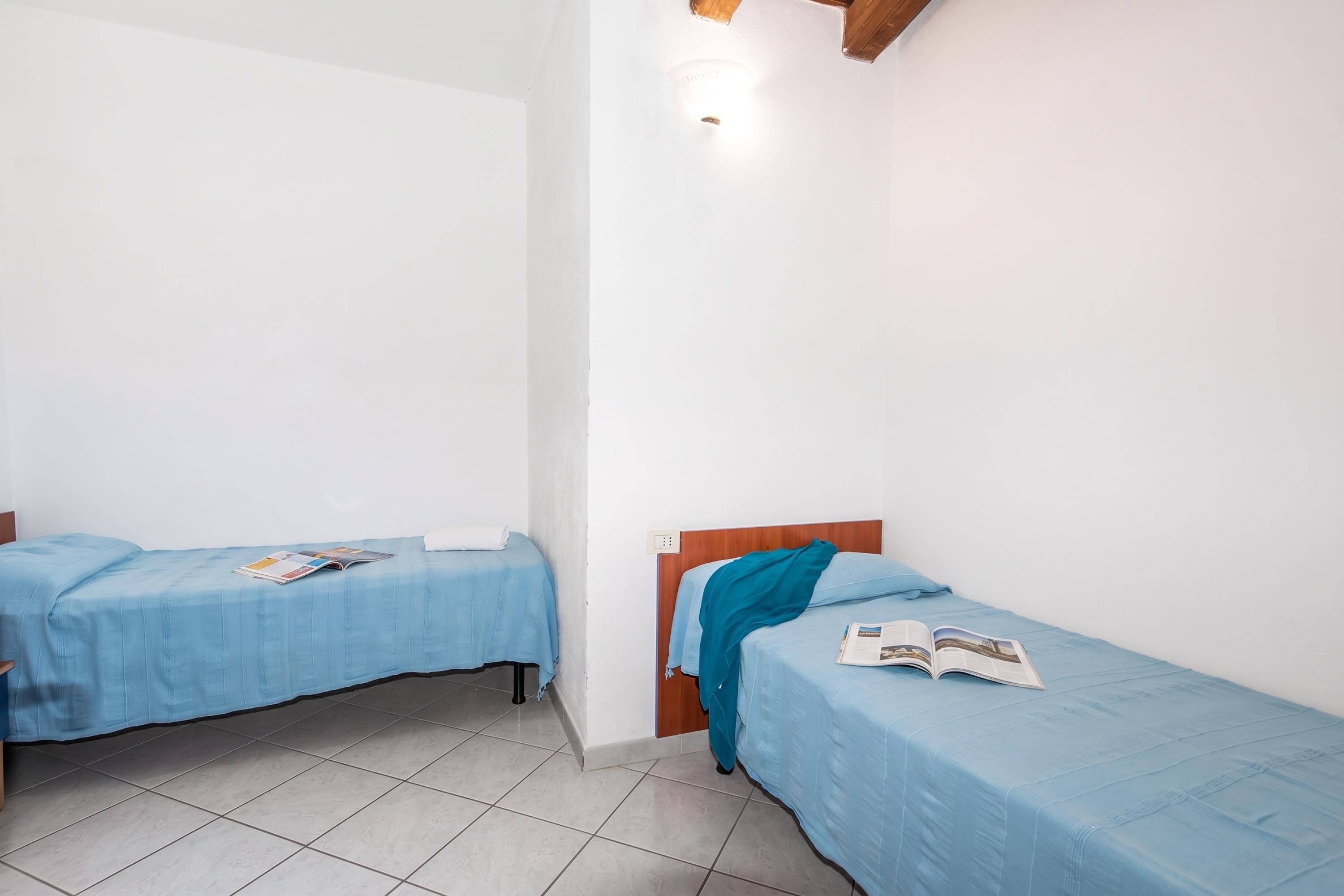 Une chambre avec deux lits simples, chacun recouvert d’une couverture bleue et agrémenté d’un magazine posé sur le lit.
