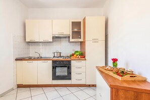 A compact kitchen with a stove, oven, and a wooden countertop with fresh produce and pastries. - Tavolara Sea View Apartments 2, San Teodoro, Italy (San Teodoro)