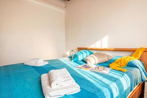 A neatly made bed with a blue bedspread, a folded white towel, and a yellow garment on the bed. - Tavolara Sea View Apartments 2, San Teodoro, Italy (San Teodoro)