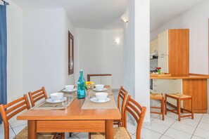 A dining area with a wooden table set for four, a kitchen in the background, and a framed picture on the wall. - Tavolara Sea View Apartments 1, San Teodoro, Italy (San Teodoro)
