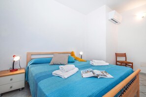 A neatly made bed with blue bedding, a wooden headboard, and a nightstand with a lamp. - Tavolara Sea View Apartments 1, San Teodoro, Italy (San Teodoro)