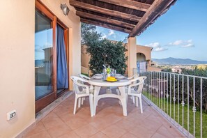 A balcony with a table set for dining, surrounded by white chairs, a view of the landscape, and a pergola overhead. - Tavolara Sea View Apartments 1, San Teodoro, Italy (San Teodoro)