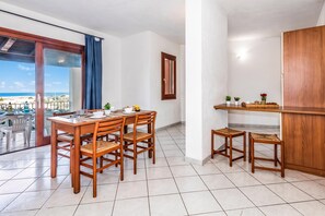 A modern dining area with a wooden table and chairs, a view of the beach, and a kitchen area with stools and a wooden cabinet. - Tavolara Sea View Apartments 1, San Teodoro, Italy (San Teodoro)