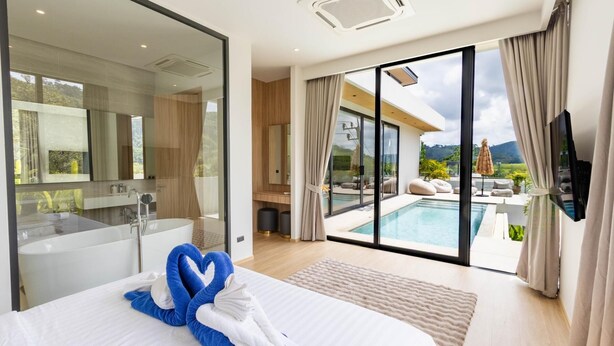 A modern hotel room with a large bed, a bathroom, a pool, and a view of the outdoors. - Aileen P3 V4 Saku Staycation (Sa Khu - Thalang)