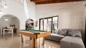Ein Billardtisch in einem Raum mit Backsteinwand, einer Couch und einem Essbereich.