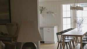 Una sala de estar con un sofá, una mesa con lámpara y un comedor con sillas.