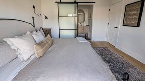 Un dormitorio con una cama grande, una puerta corredera al baño y un cuadro en la pared.