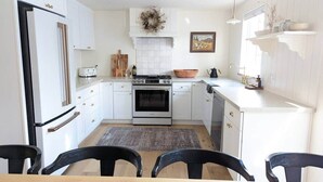 Cocina compacta con muebles blancos, horno integrado y comedor con mesa y sillas.