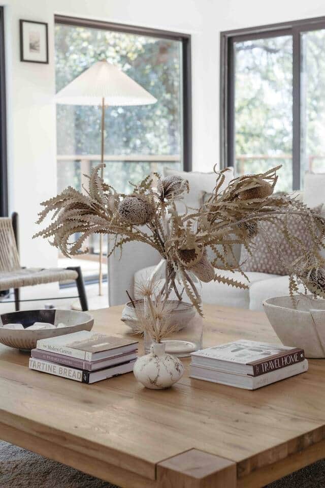 Ein Holztisch mit Dekoration, Büchern und einer Vase mit Trockenpflanzen.