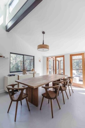 Un vaste espace dédié à la salle à manger, avec une longue table en bois et six chaises, de grandes fenêtres et un design moderne au niveau du plafond.