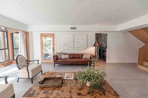 Un salon spacieux avec un canapé en cuir, une table basse agrémentée d’une plante et une vue sur l’extérieur grâce à de grandes fenêtres.