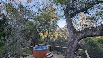 Un jacuzzi en una terraza de madera rodeado de árboles.