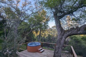 Un bain à remous sur une terrasse en bois, entouré d’arbres.