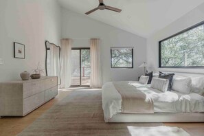 Une chambre à coucher avec un lit, une commode, un ventilateur de plafond et une grande fenêtre.