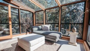 A bedroom with a large window, a bed, a bench, and a small table. - Skog Dom | Retreat in the Trees | Hot Tub | Auburn (Placer County)