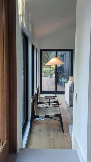 Un couloir mène à un patio aménagé avec une table et des chaises, de grandes fenêtres et une vue sur l’extérieur.