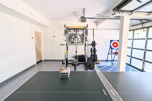 Une salle de sport équipée d’un support à squats, de disques de poids, d’un banc et d’une cible pour s’entraîner au tir.