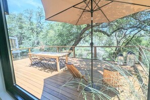 Une terrasse en bois avec une table et des chaises, entourée de verdure.
