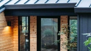 A modern house with a sloped metal roof, large glass doors, and a wooden deck with pumpkins. - Skog Dom | Retreat in the Trees | Hot Tub | Auburn (Placer County)