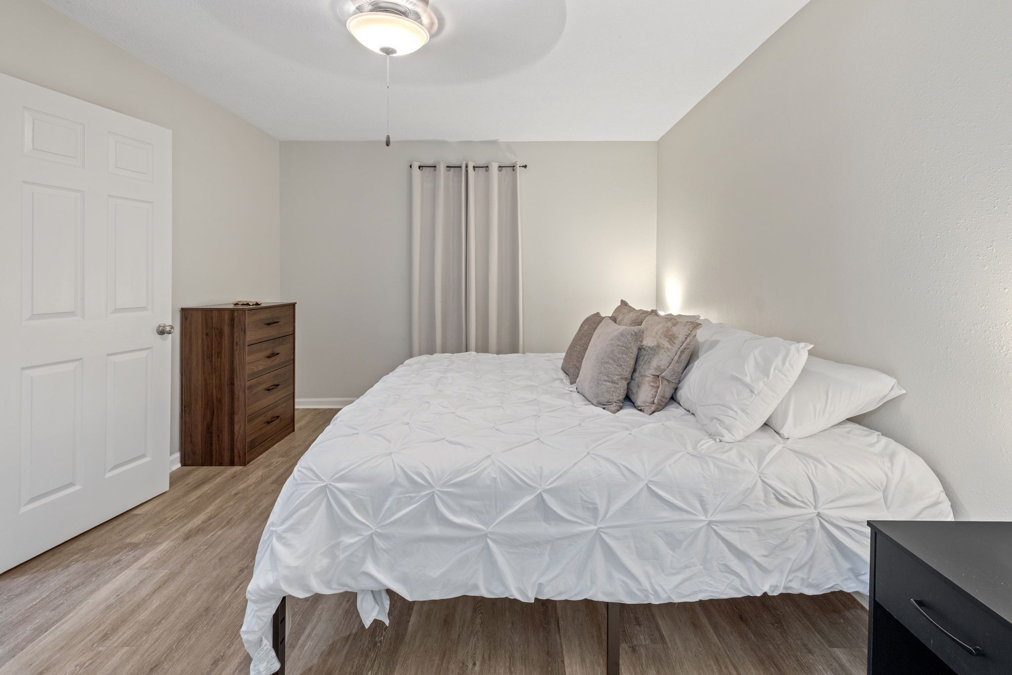 Une chambre à coucher avec un lit, une commode, un ventilateur de plafond et une porte.