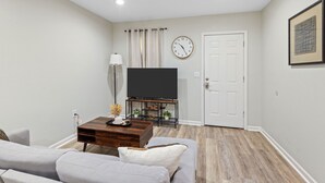 Una sala de estar con un sofá, una mesa de centro, un televisor, un reloj y una puerta.