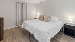 Un dormitorio con cama, mesitas de noche, un armario de madera y una ventana con cortinas.