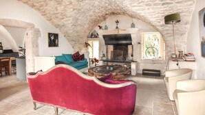A room with a stone ceiling, a fireplace, a red sofa, and a dining area. - Maison avec piscine privée (Clansayes)