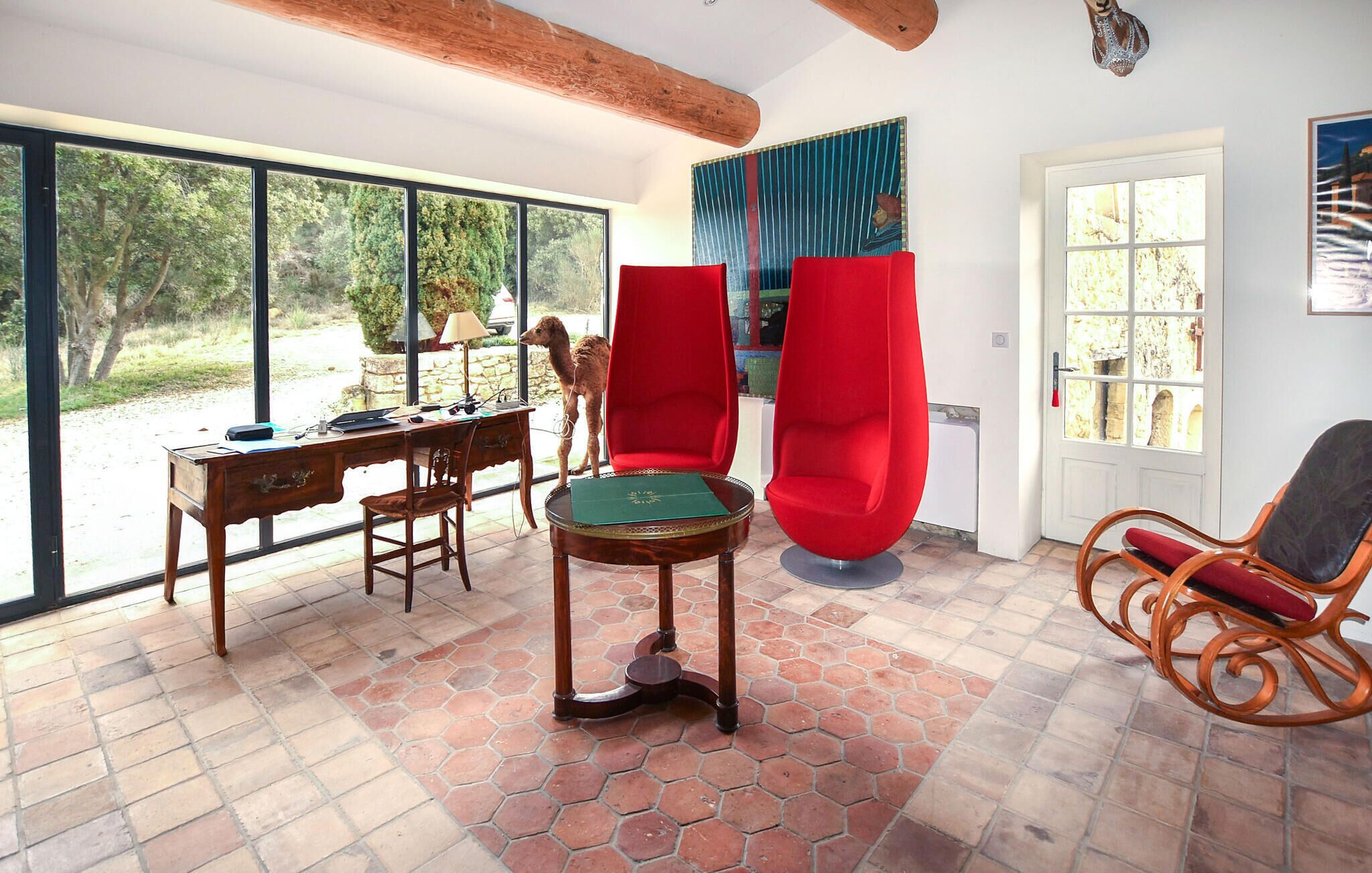 A room with a desk, two red chairs, a round table, and large windows.
