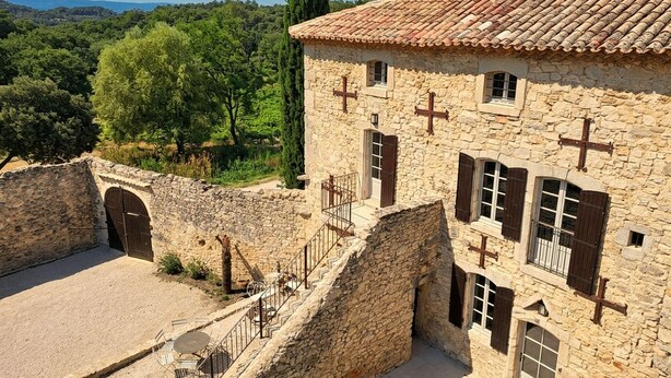 A stone building with a tiled roof, a staircase leading to an upper level, and a view of the surrounding landscape. - Maison avec piscine privée (Clansayes)