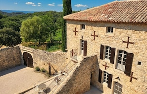 Un bâtiment en pierre avec un toit en tuiles, un escalier menant à un étage supérieur et une vue sur le paysage environnant.