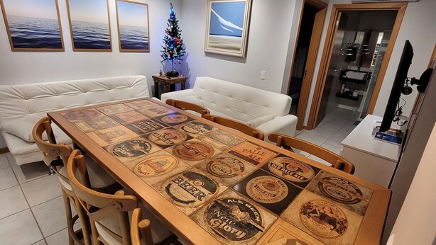 Un espace repas avec une longue table en bois, plusieurs chaises, un petit sapin de Noël et des œuvres d’art murales.