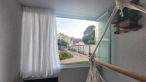 Un balcon donnant sur une rue résidentielle, un hamac et une petite table sur laquelle sont posés divers objets.