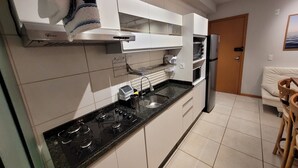 Une cuisine moderne avec des meubles blancs, un plan de travail noir, une cuisinière, un four à micro-ondes et un réfrigérateur.