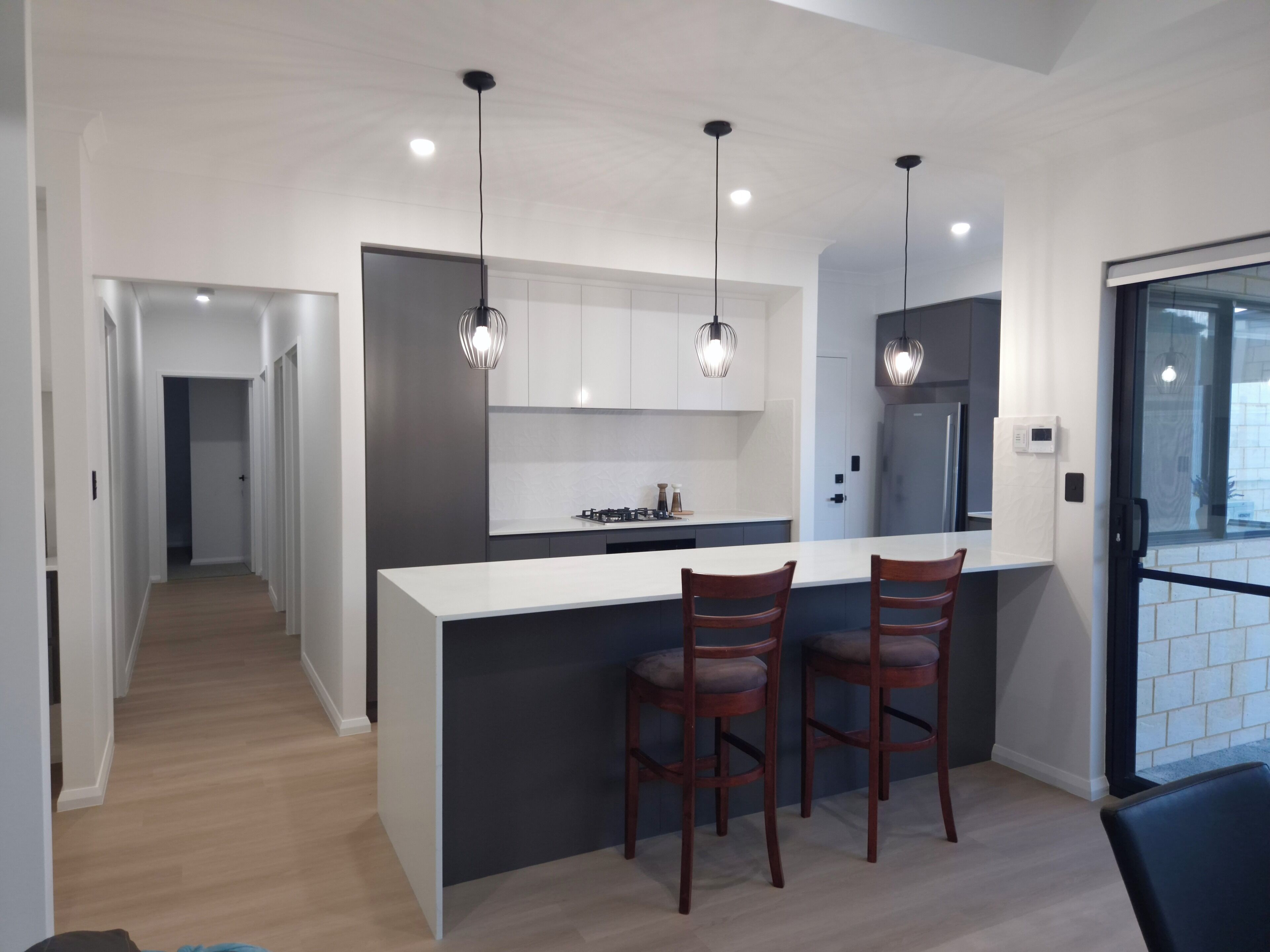 Une cuisine moderne dotée d’un îlot central, de luminaires suspendus et offrant une vue sur l’extérieur.