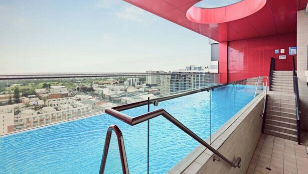 A rooftop swimming pool with a glass barrier, a red ceiling, and a view of the cityscape. - Two Bedroom Unit in Central Adelaide (City of Adelaide)