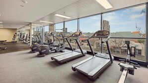 A gym with treadmills, weight machines, and a large window with a city view. - Two Bedroom Unit in Central Adelaide (City of Adelaide)