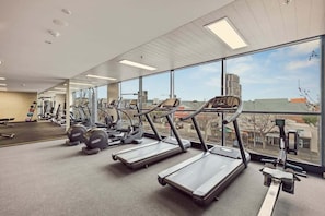 A gym with treadmills, weight machines, and a large window with a city view.