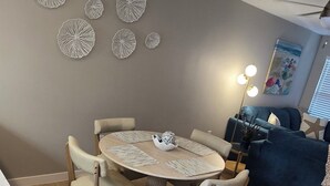 Een eethoek met een ronde tafel en stoelen, een plafondlamp, wanddecoratie en een bank op de achtergrond.