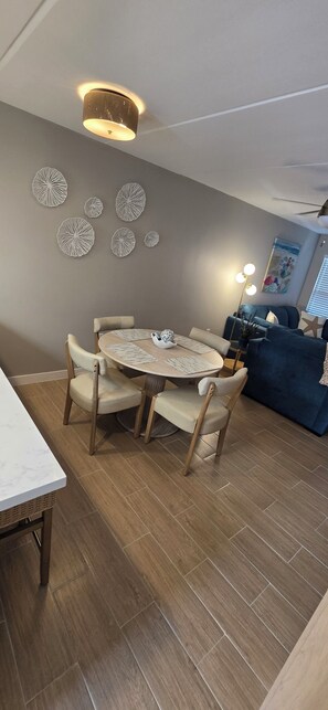 Ein Essbereich mit rundem Tisch und Stühlen, einer Deckenleuchte, Wanddekoration und einer Couch im Hintergrund.