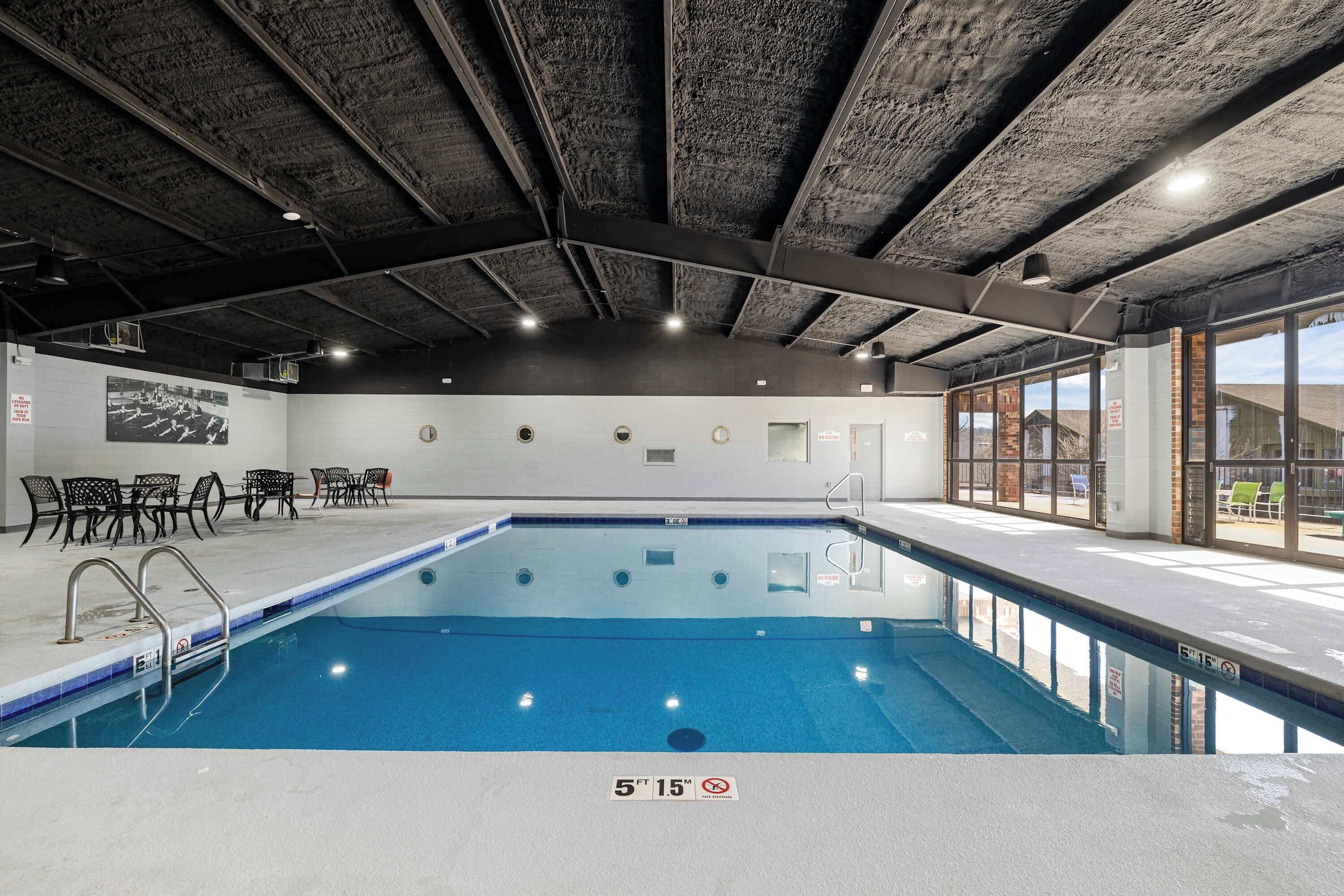 Une piscine intérieure dotée d’un plafond en béton, de chaises placées au bord du bassin et offrant une vue sur l’extérieur.