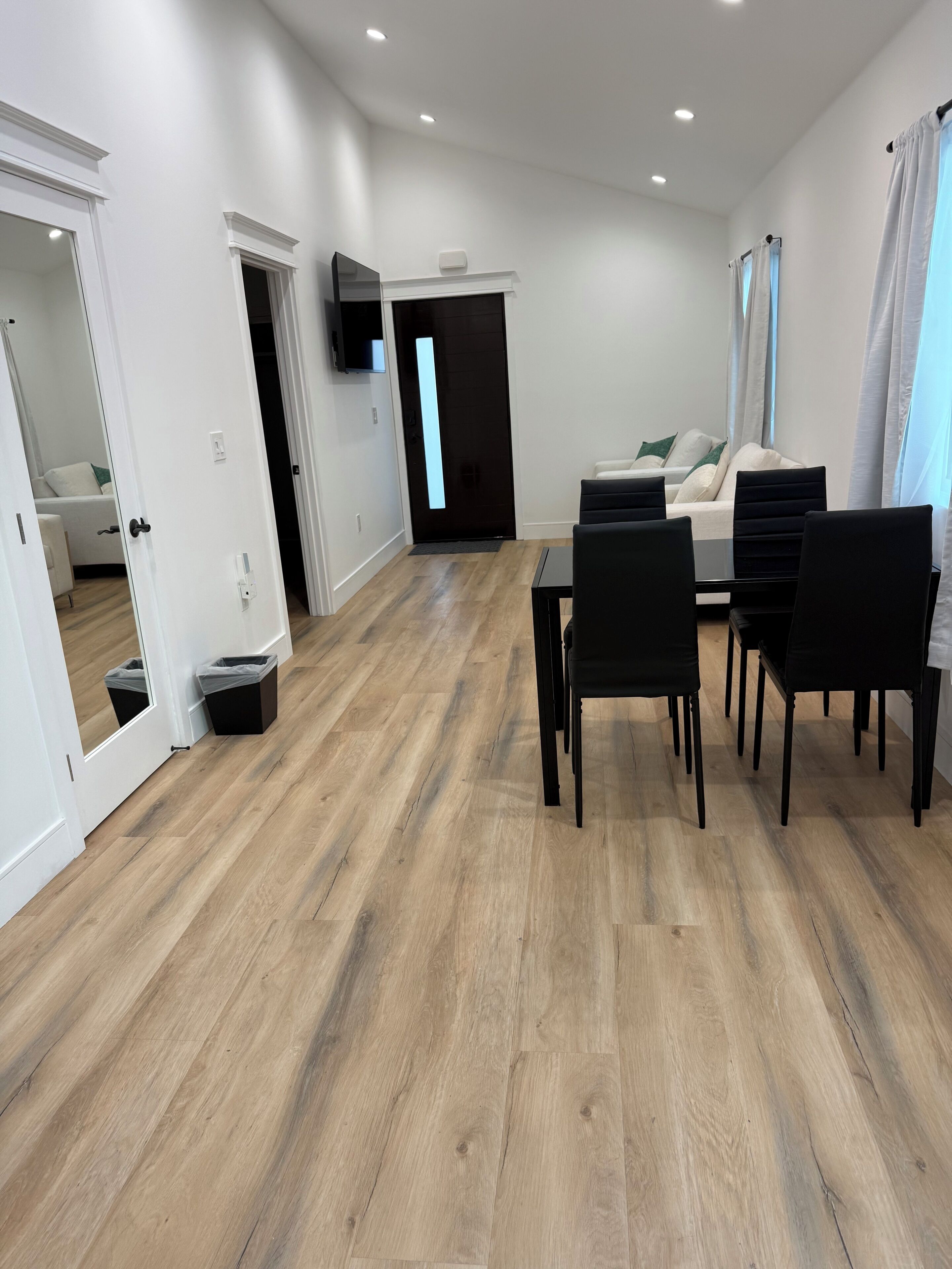 A modern living room with a dining area, wooden flooring, white walls, and a flat-screen TV mounted on the wall.