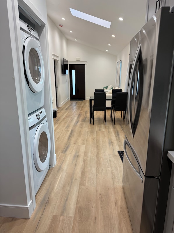 A modern kitchen with stainless steel appliances, a dining area with a table and chairs, and a laundry area with a washing machine.
