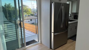 A modern kitchen with a stainless steel refrigerator, a sliding glass door leading to a backyard, and light-colored wooden flooring. - Perfect 2-bedroom corporate apartment with AC in peaceful Altadena (Altadena)