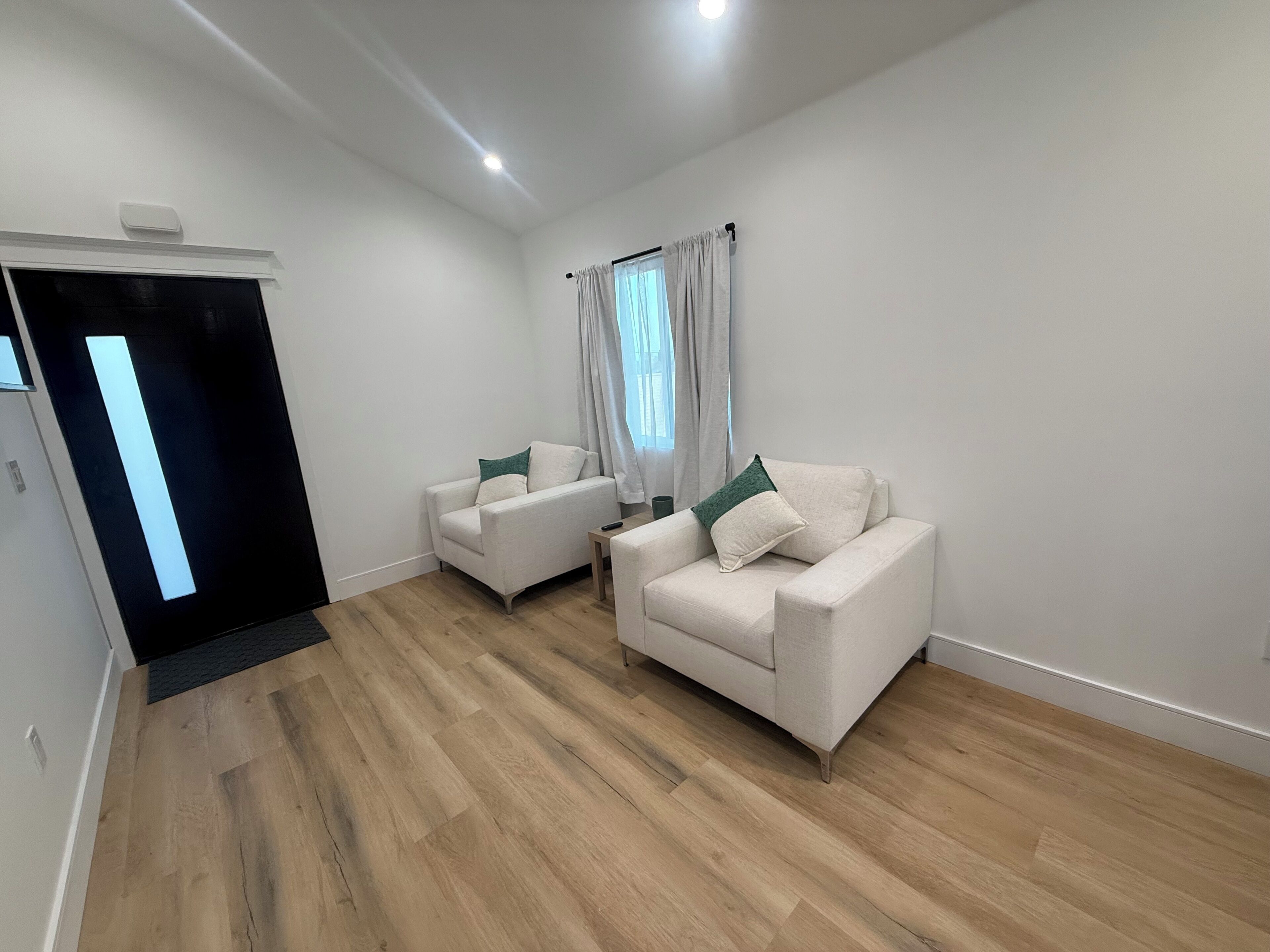 A modern living room with two white sofas, a wooden floor, and a large window with curtains.