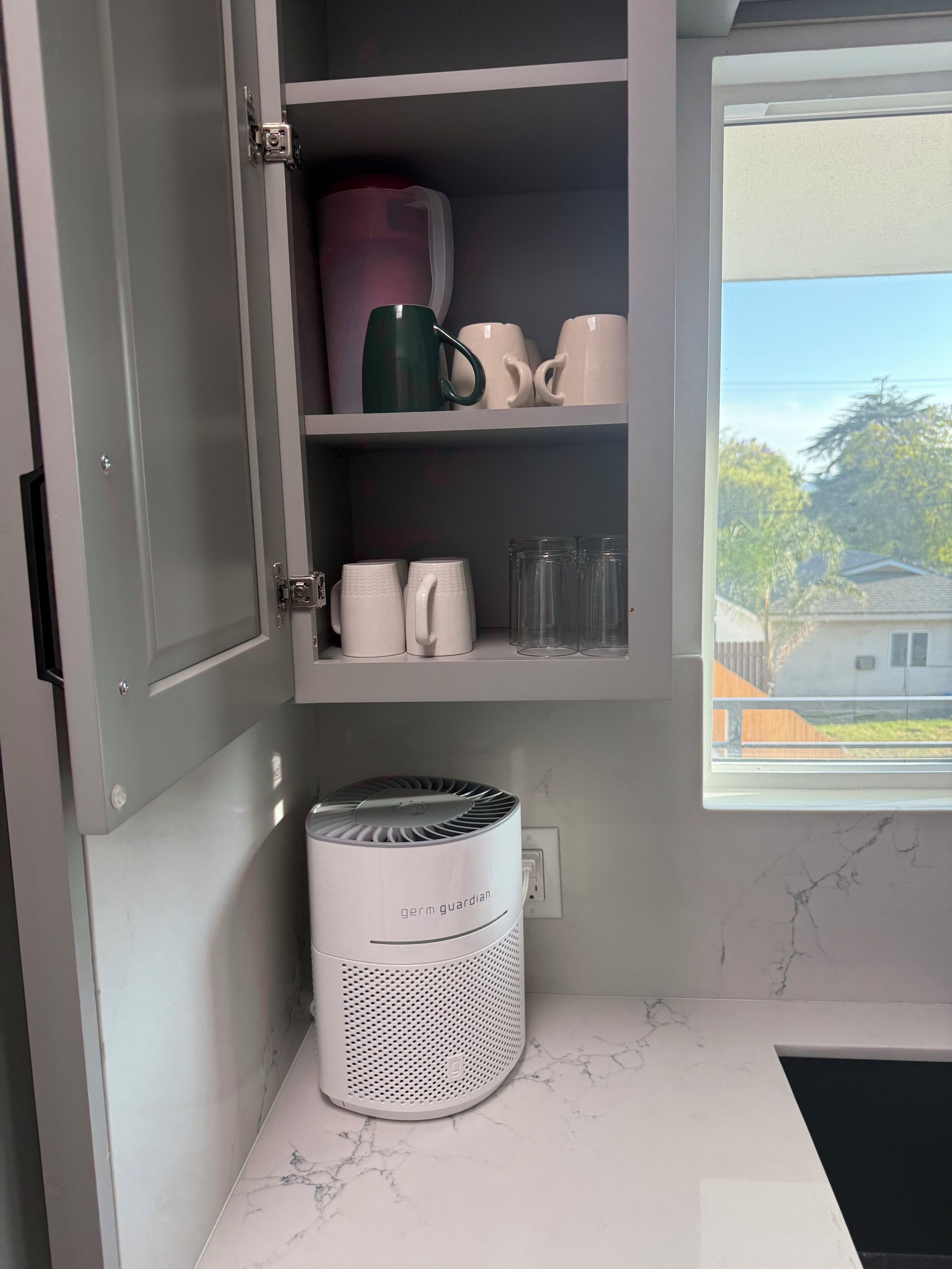 A kitchen with a built-in cabinet, a window with a view, and a white appliance on the counter.