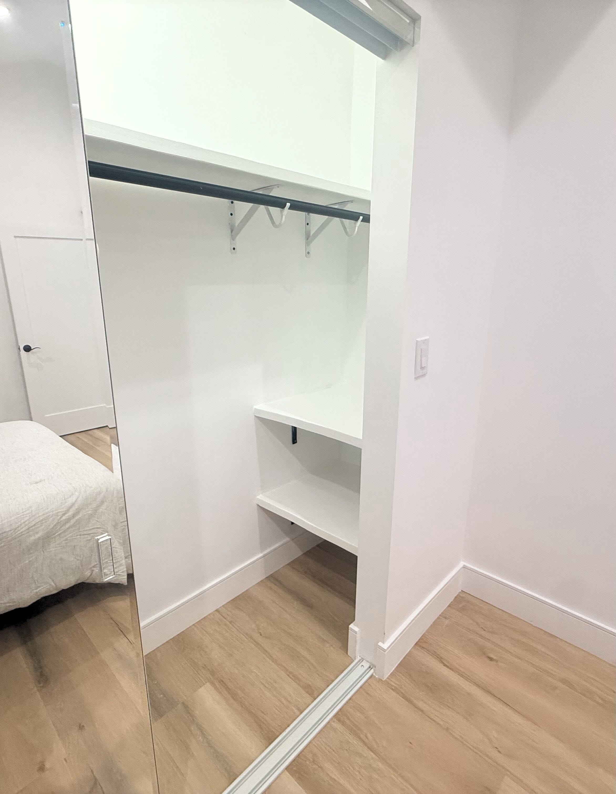 Une pièce avec un lit, une armoire blanche, un plancher en bois et un mur blanc.