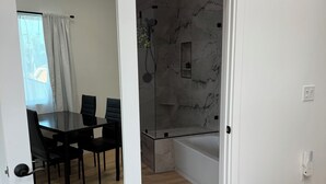 A modern bathroom with a glass-enclosed shower, marble walls, and a small shelf. - Perfect 2-bedroom corporate apartment with AC in peaceful Altadena (Altadena)