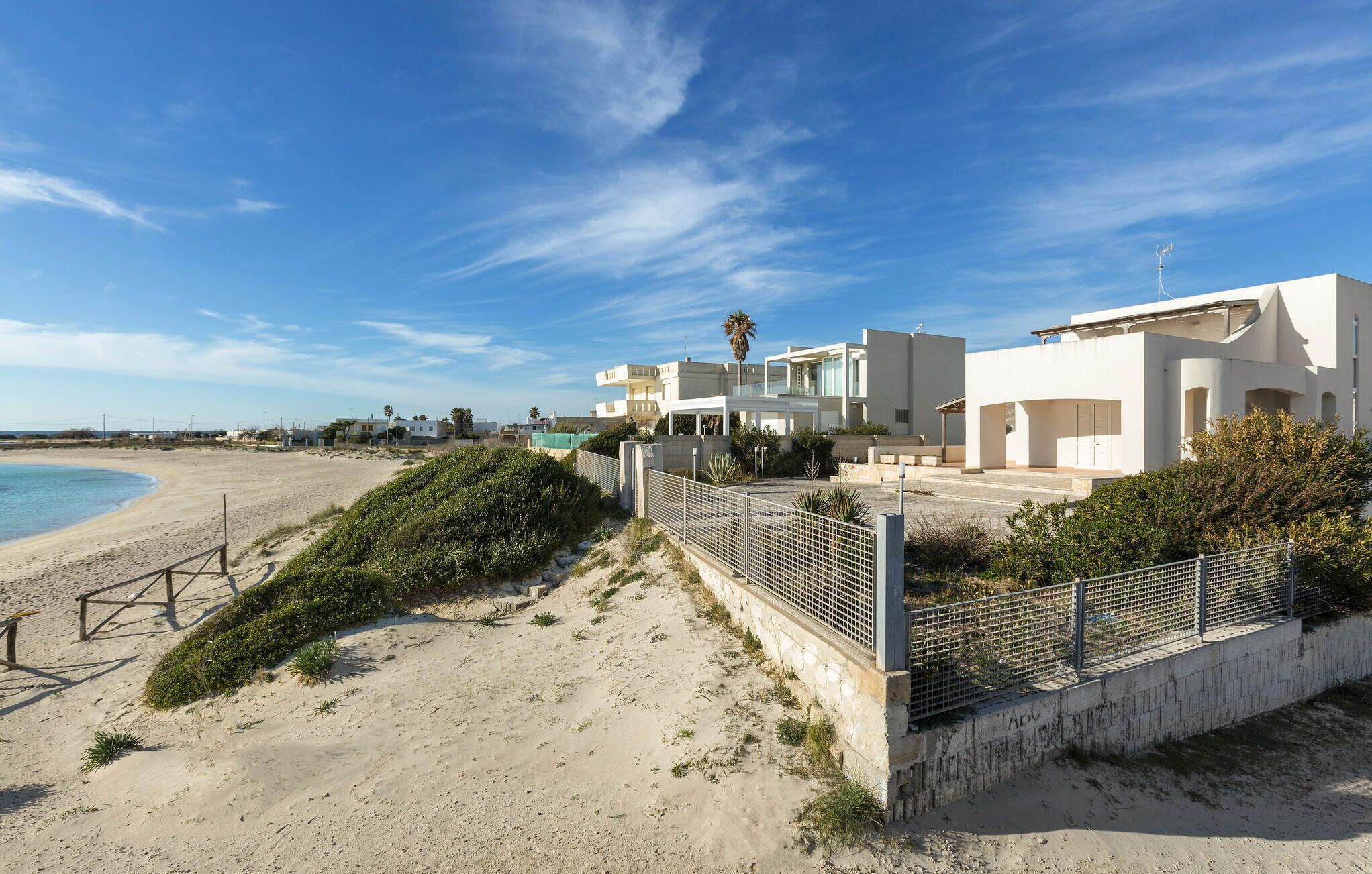 Una propiedad costera con playa de arena, zona vallada y edificios blancos modernos.